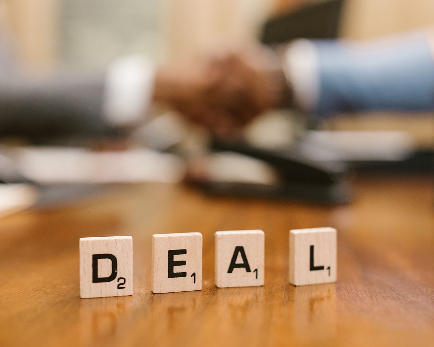 Two people shaking hands across a desk after agreeing terms